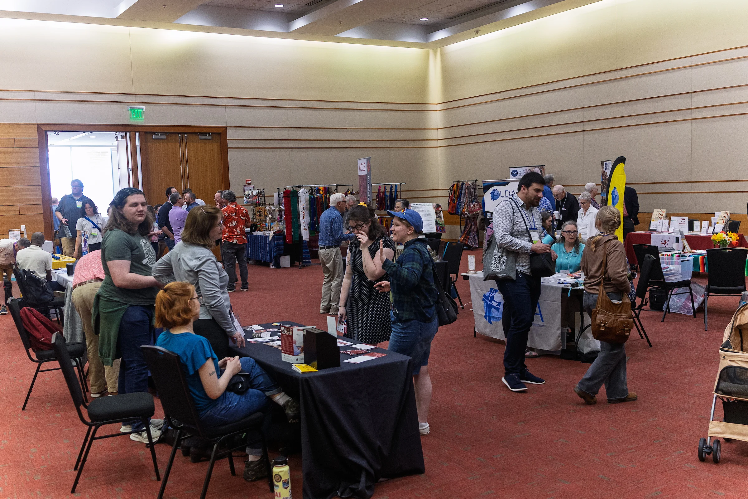People browse tables and chat at an indoor event or convention with displays and booths, gathering valuable resources and insights curated by the Institute of Liturgical Studies.