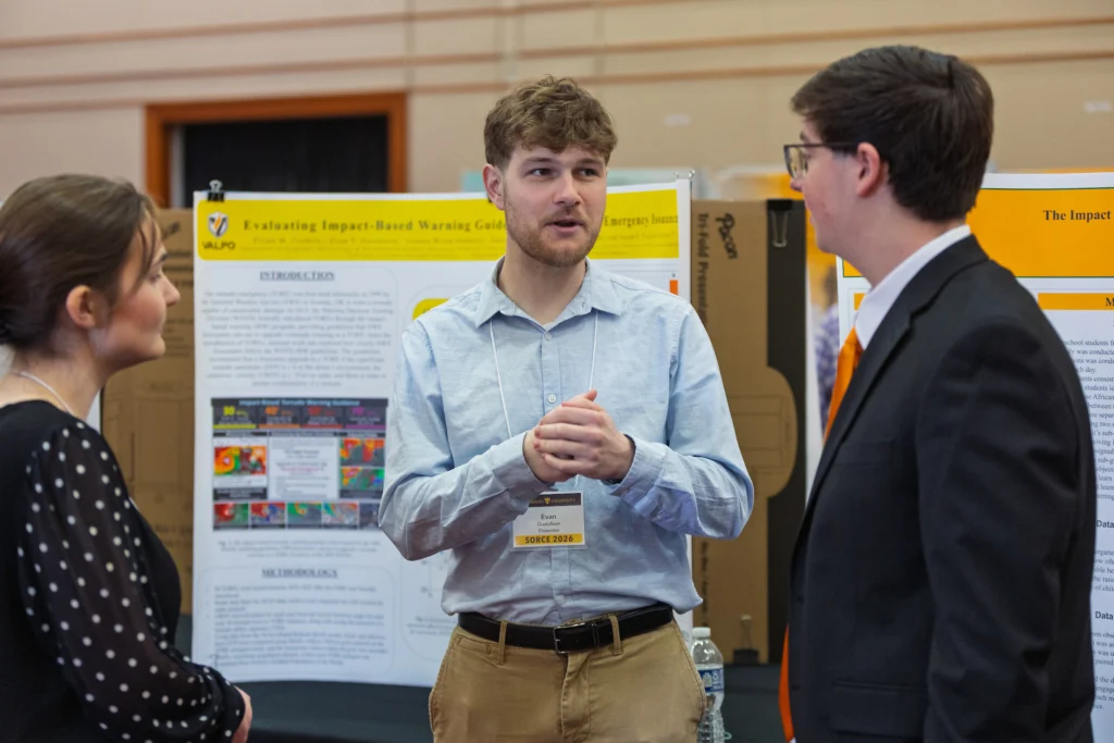 Three people are talking in front of scientific posters at a research conference or academic event. As Valparaiso University meteorologists, they are discussing effective tornado emergency guidelines and sharing insights on how their research contributes to public safety.