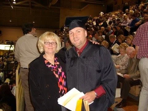 A graduate in cap and gown stands next to a woman in a crowded indoor graduation ceremony at Valparaiso University.