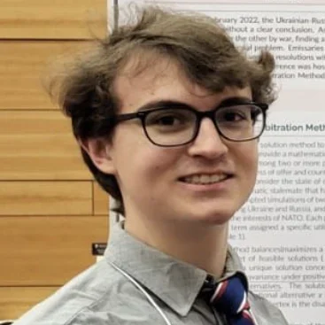 Valparaiso University student with glasses and a striped tie stands in front of a poster presentation.