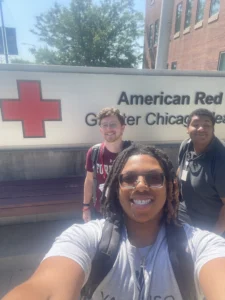 Three people smiling in front of an American Red Cross Greater Chicago sign on a sunny day, highlighting a memorable moment from a CAPS Fellow Story.