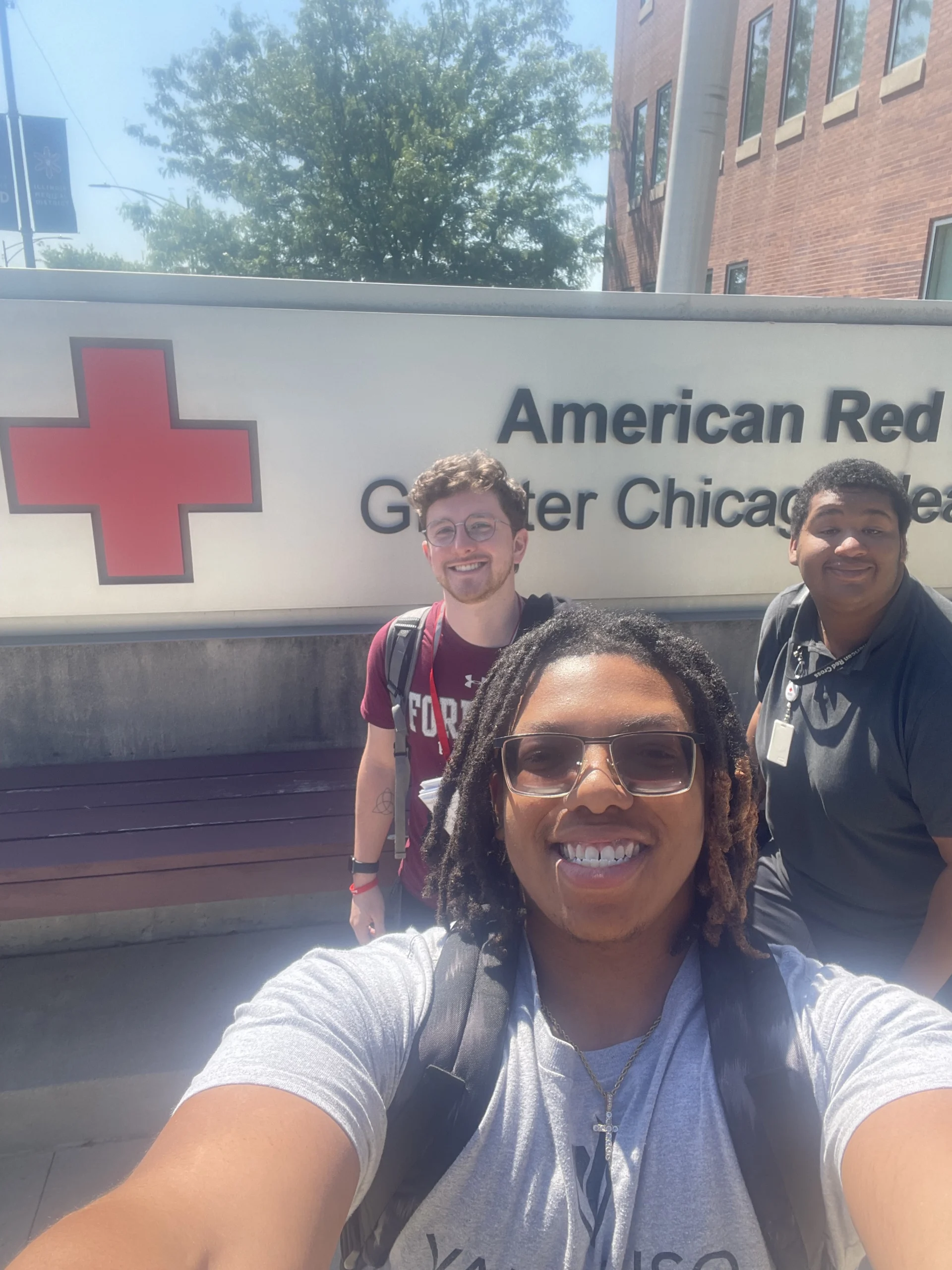 Three people smiling in front of an American Red Cross Greater Chicago sign on a sunny day, highlighting a memorable moment from a CAPS Fellow Story.
