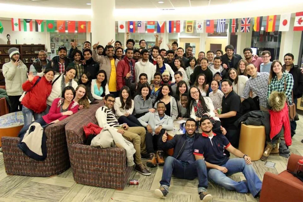 A large, diverse group of people smile and pose together in a room decorated with international flags.