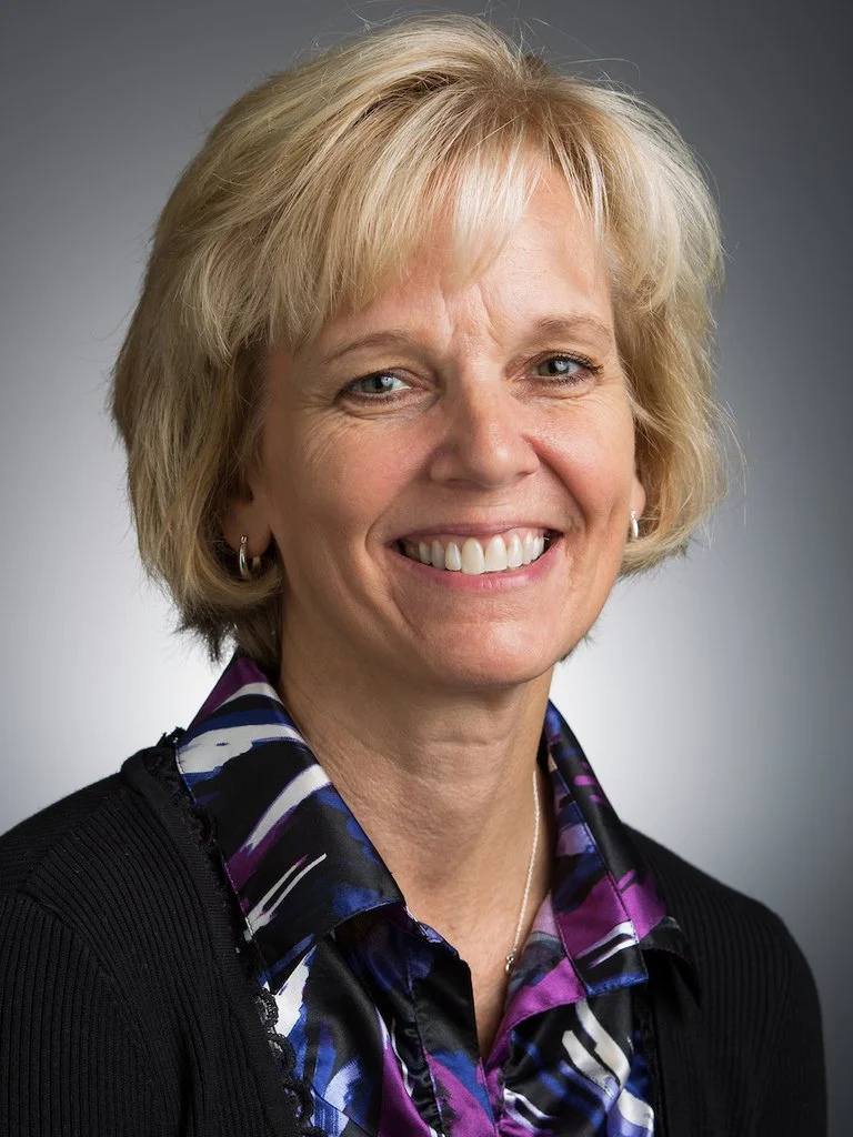 A smiling woman with short blonde hair in a black cardigan, pictured for our workshops.