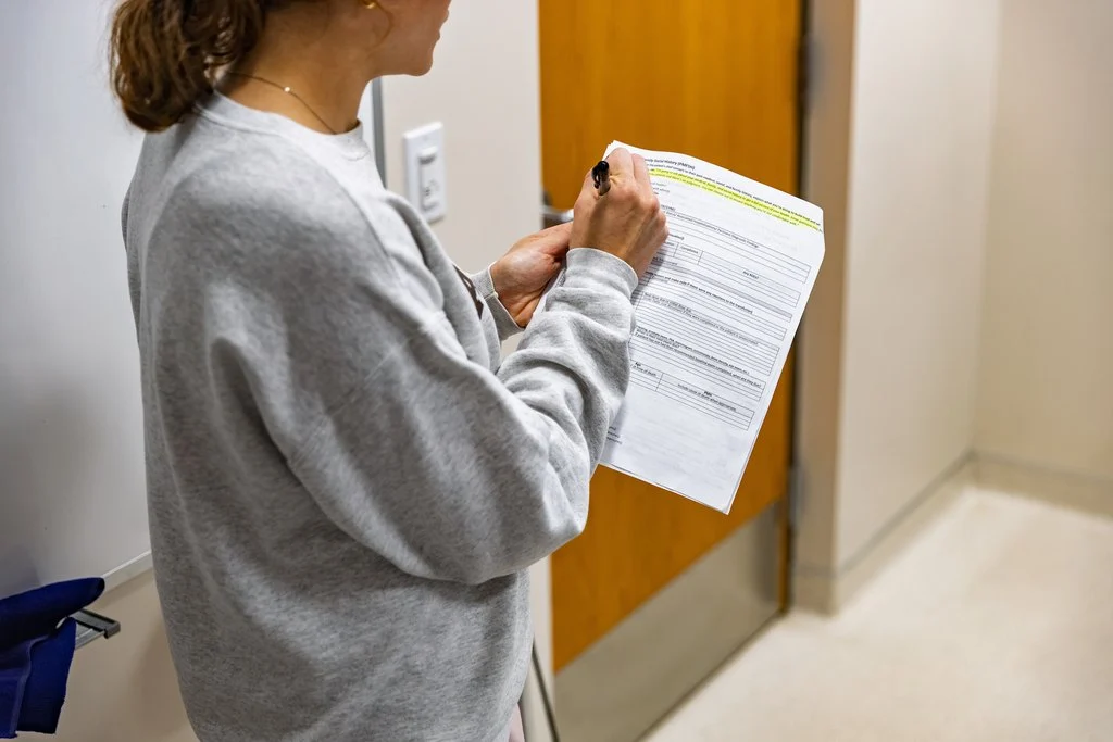 A person in a gray sweatshirt completes a clinical social history form for the Valparaiso University healthcare program.