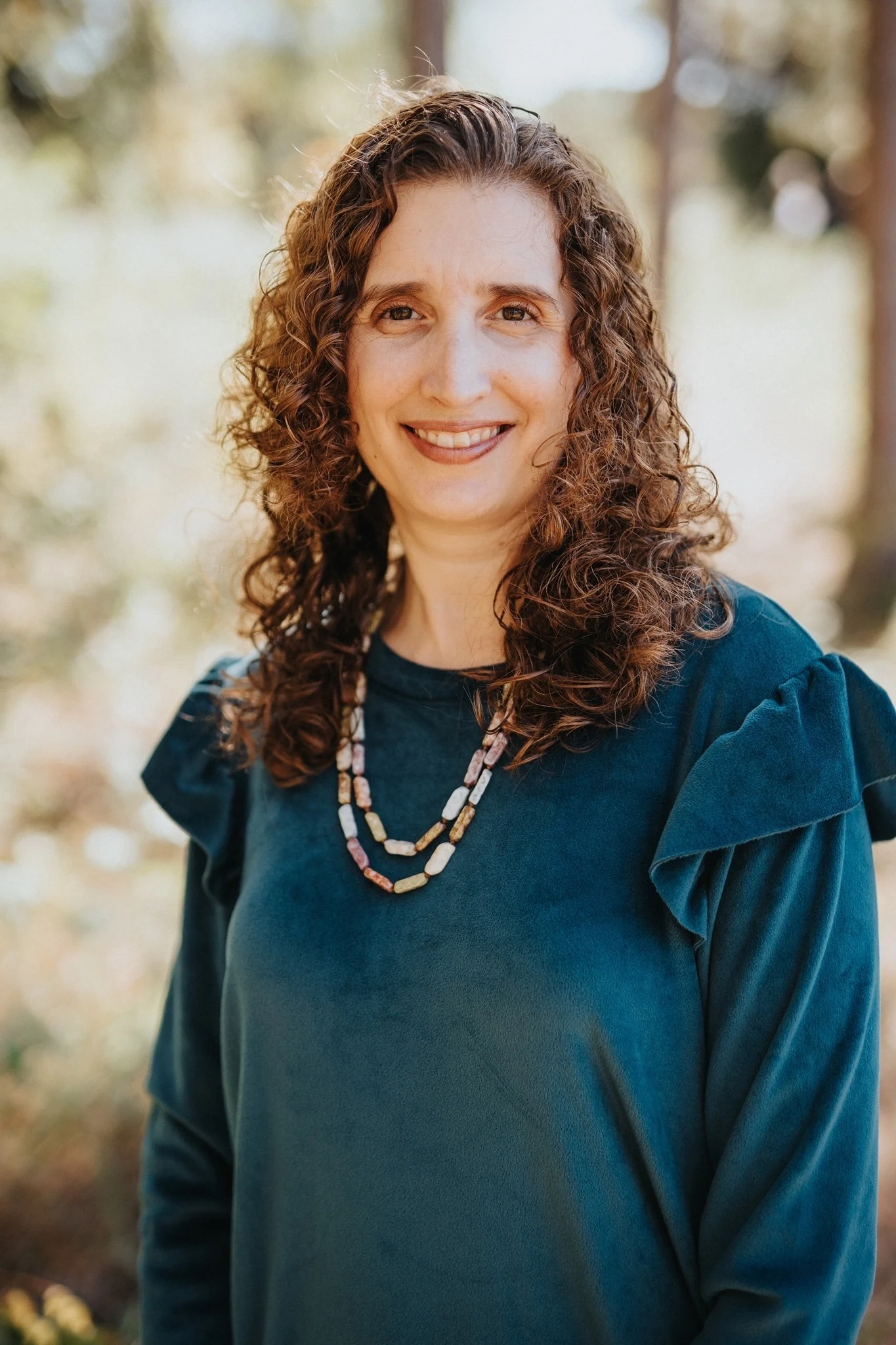A woman with long curly hair in a teal top and beaded necklace at the workshops.