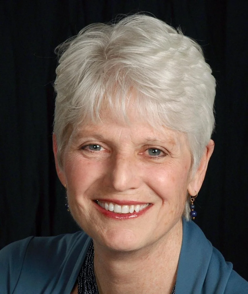 Smiling woman with short silver hair leading a workshop.