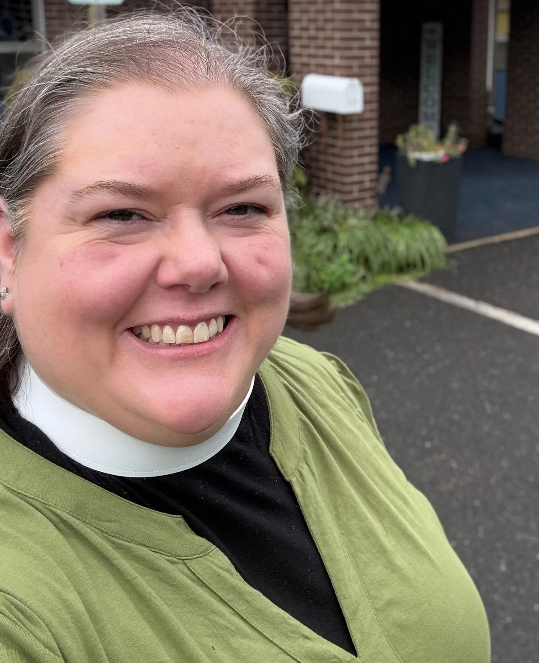 A smiling worship leader wearing a clergy collar and a green top.
