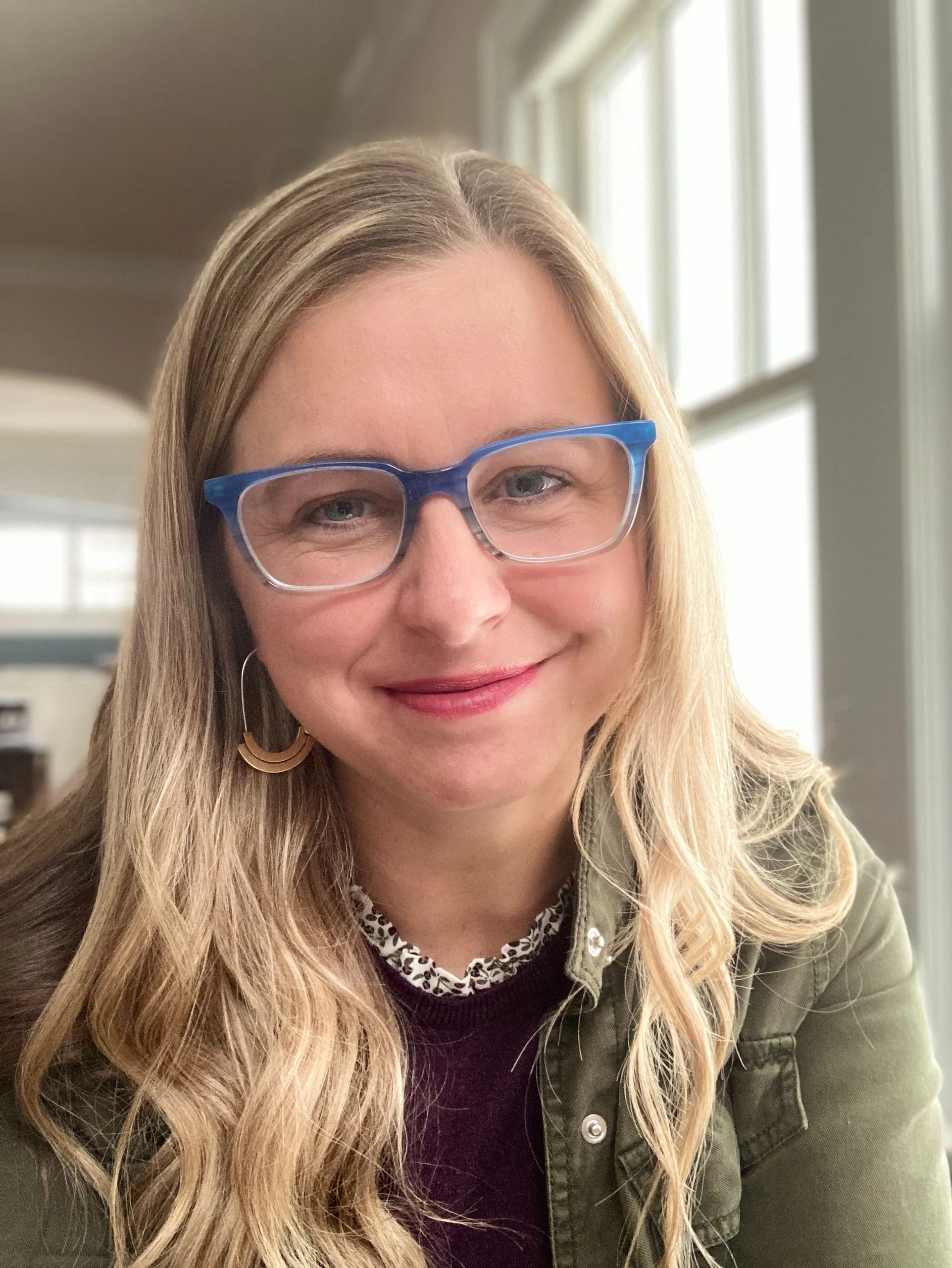 A smiling woman with blonde hair and blue-framed glasses at one of the workshops.