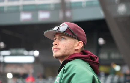 A man in a maroon baseball cap and green jacket looks upward at a Valparaiso University local baseball game.