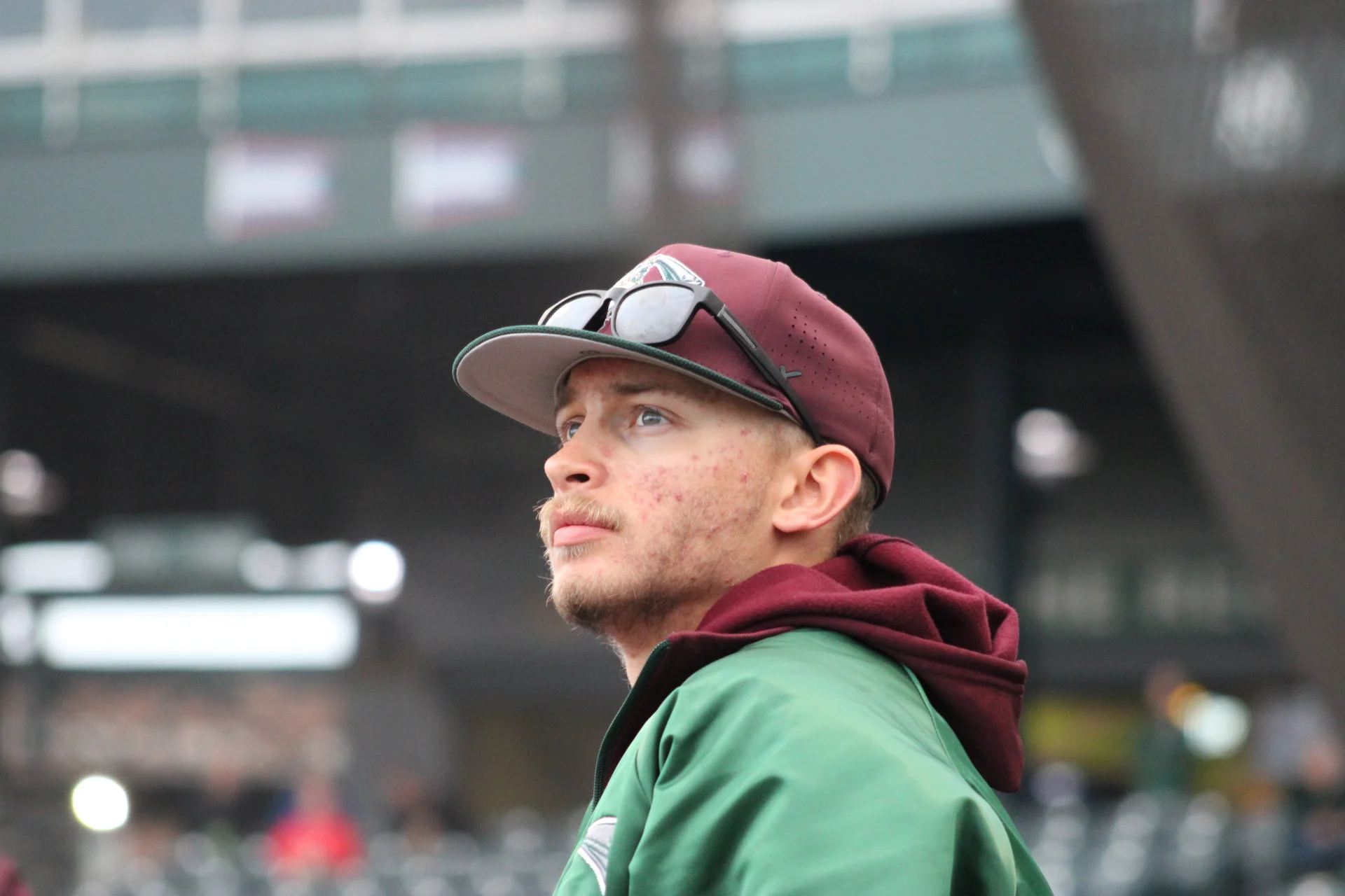 A man in a maroon baseball cap and green jacket looks upward at a Valparaiso University local baseball game.