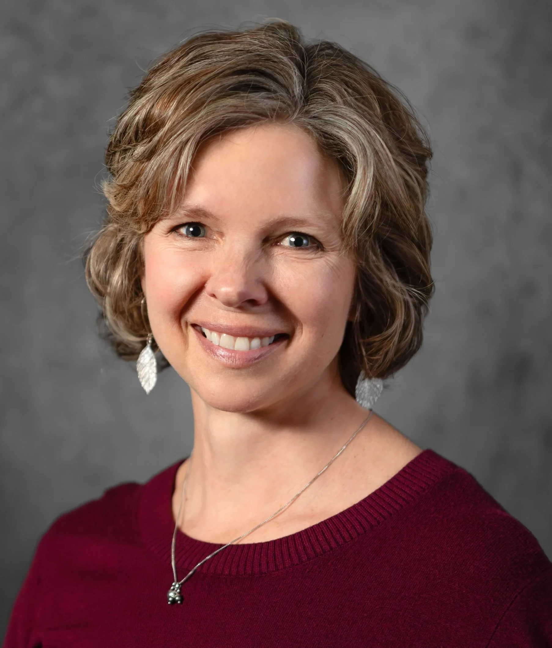 Smiling woman in a maroon sweater and silver necklace, presenting workshops.