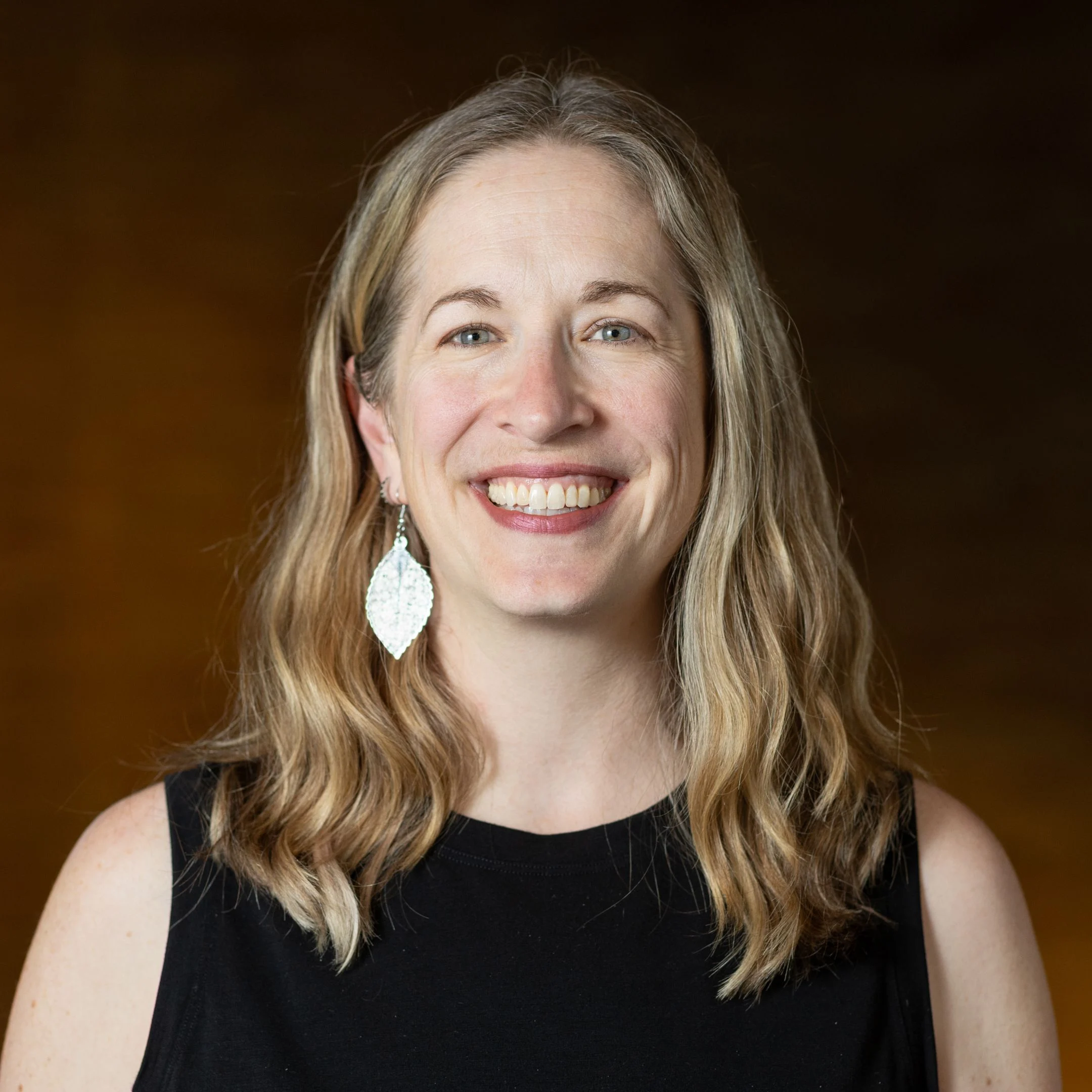 Smiling woman with shoulder-length blonde hair and leaf earrings leading workshops.