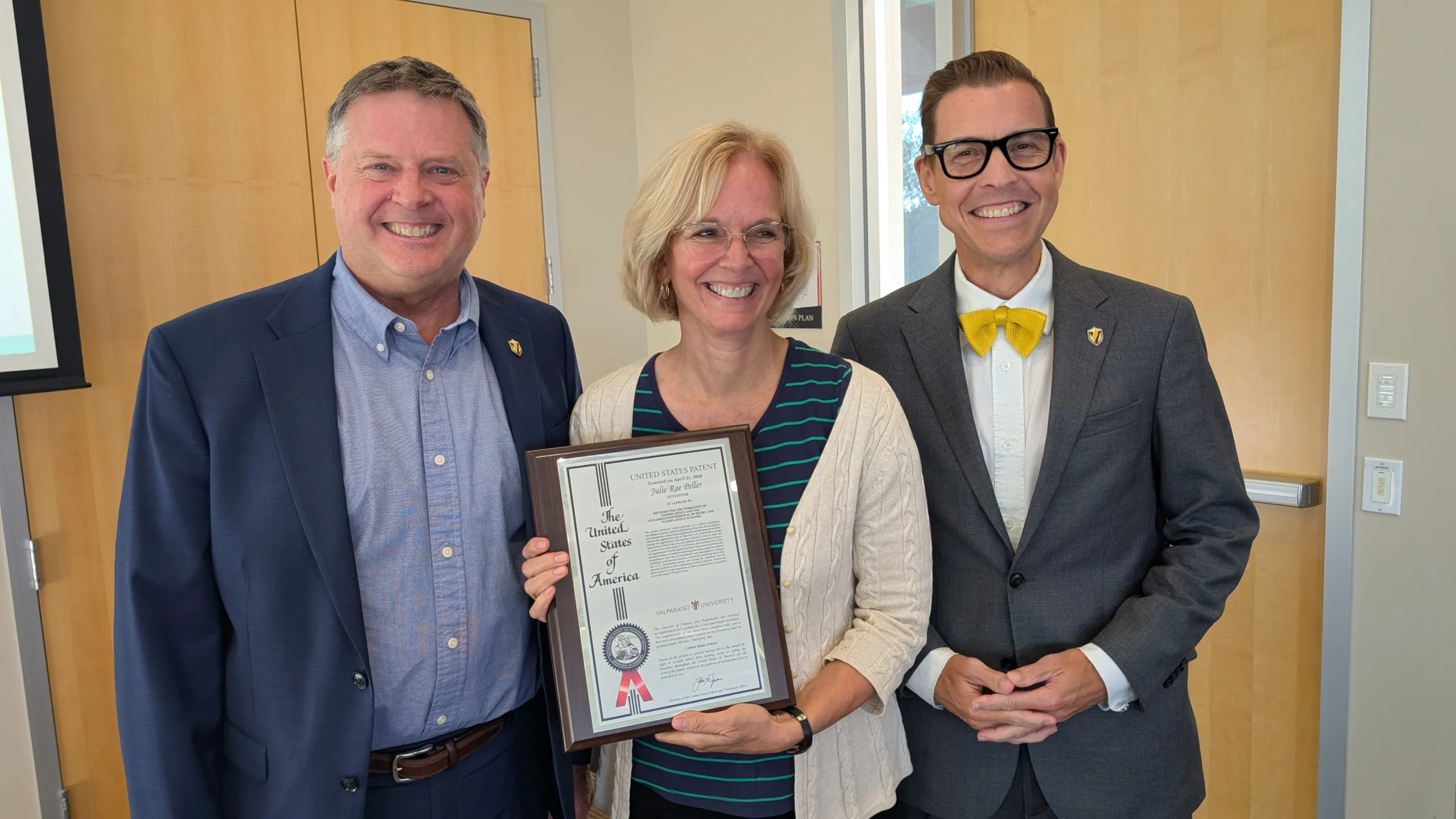 Three people smiling, with the center person holding a Valparaiso University patent for water filtration.