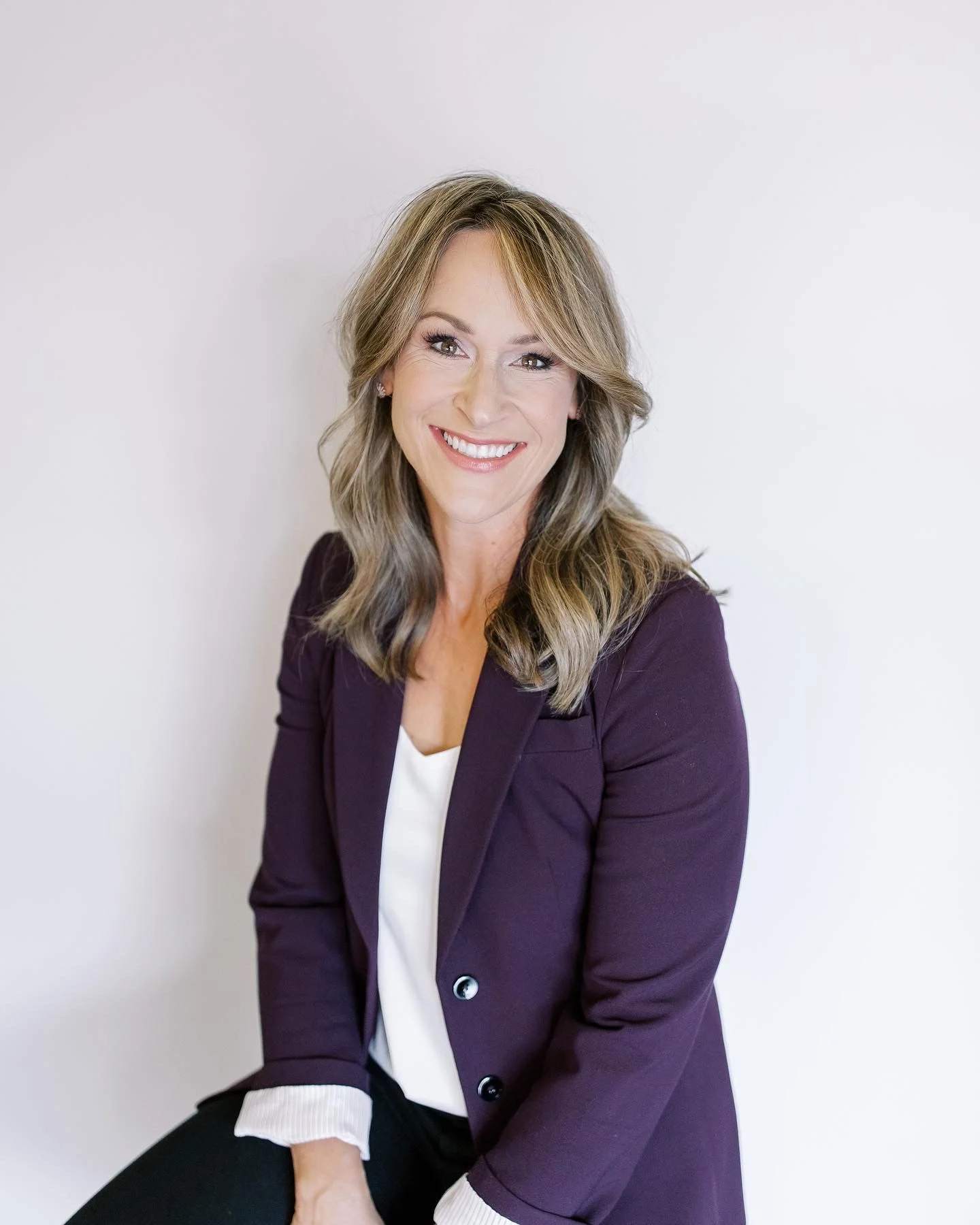 Smiling worship leader with shoulder-length hair wearing a purple blazer over a white top.
