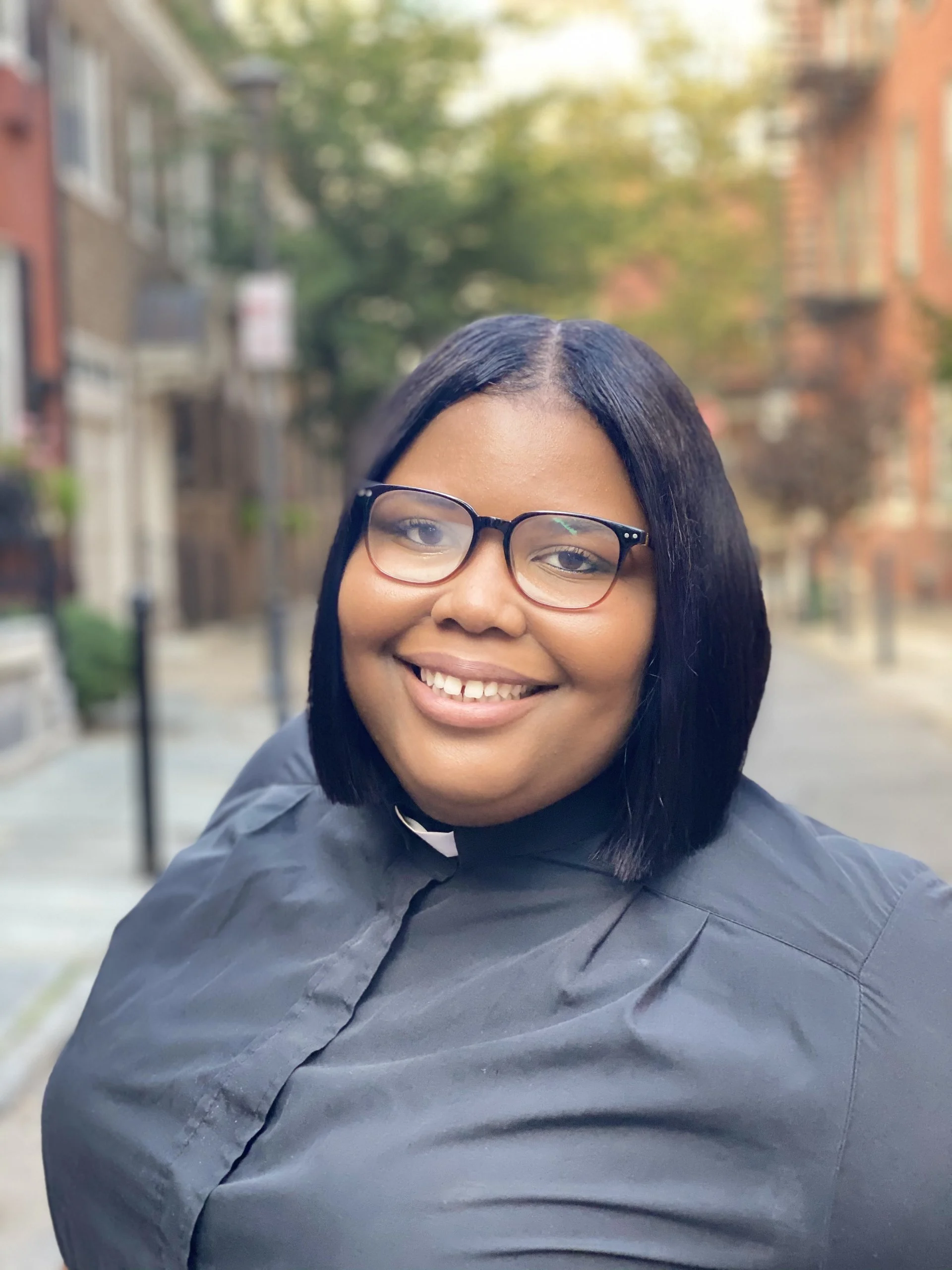 A smiling woman wearing glasses and a black clerical shirt at a workshop.