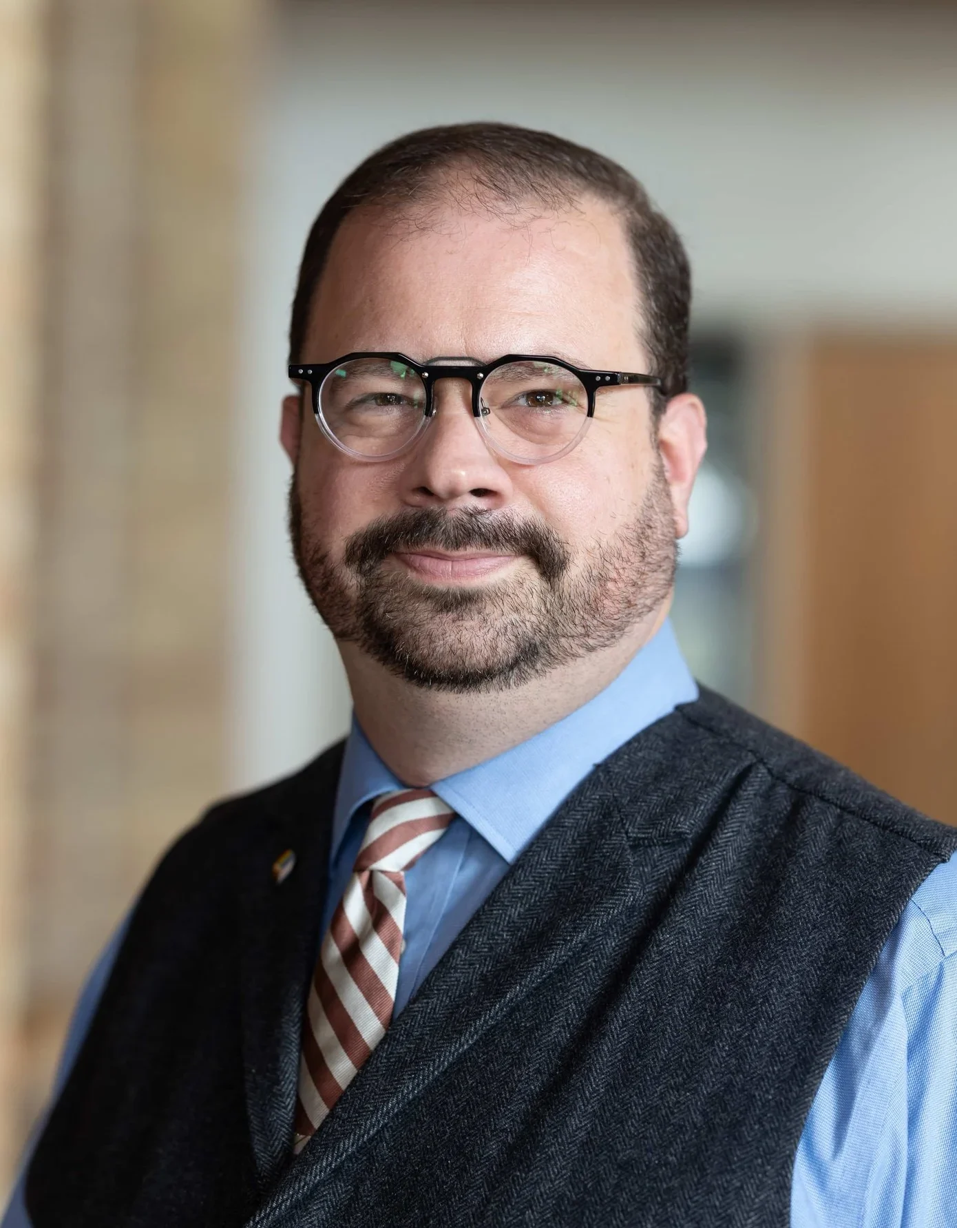 A bearded man in glasses, a blue shirt, striped tie, and dark vest leading workshops.