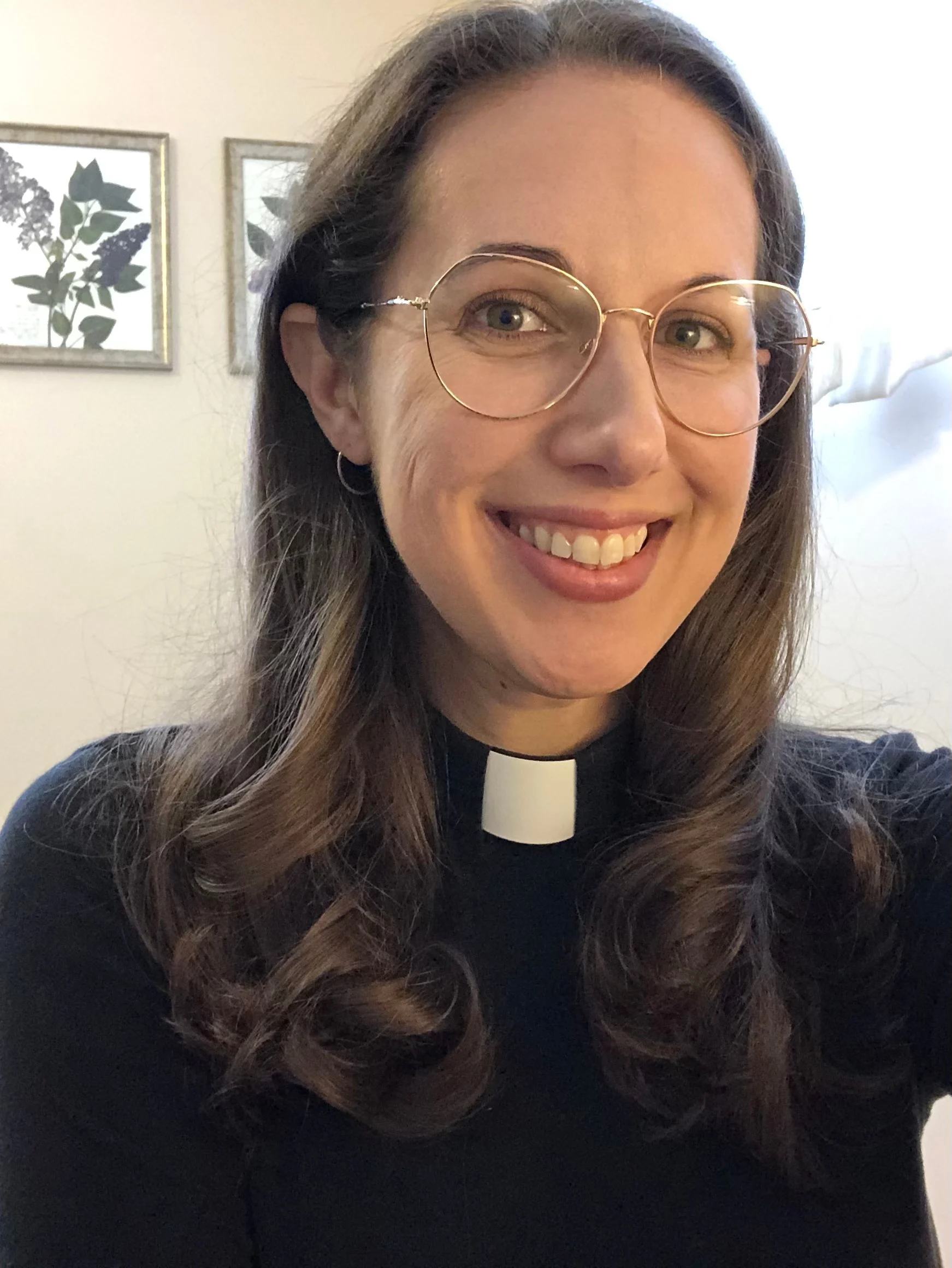 A woman in round glasses and a clergy collar smiling during a workshop.