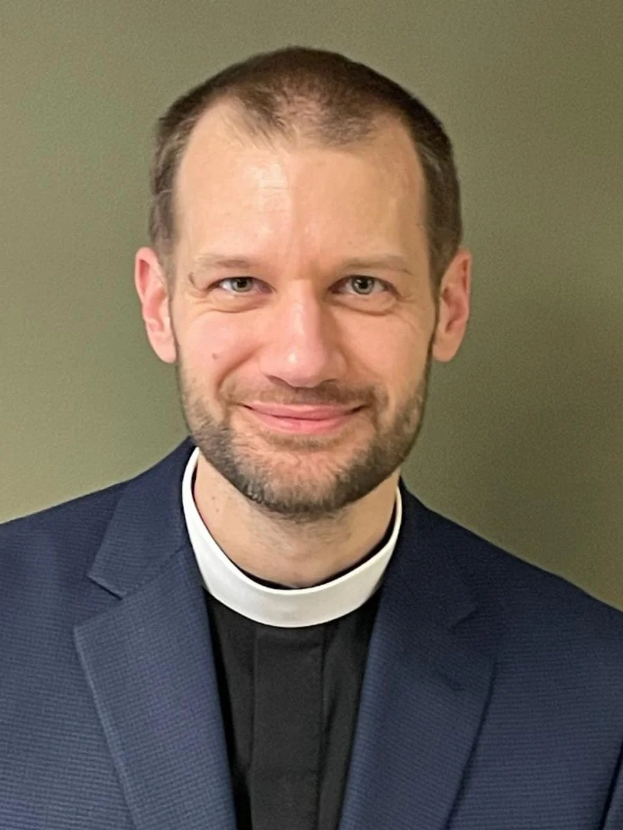 A worship leader wearing a clerical collar and a dark blazer.