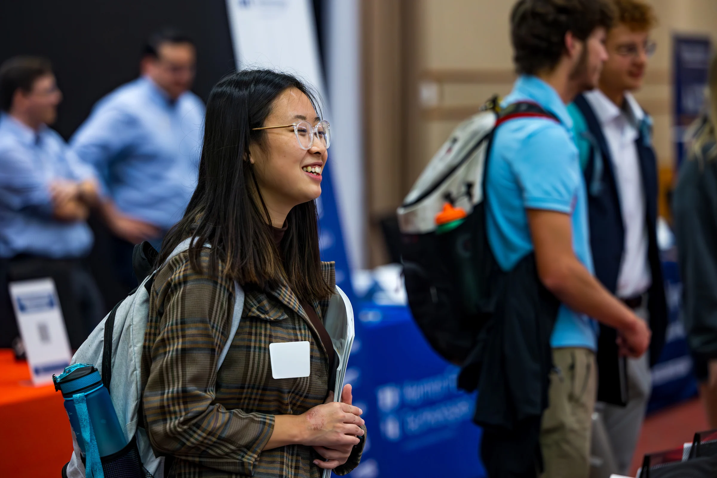 A smiling young woman in a plaid jacket and name tag attends a career guidance event.
