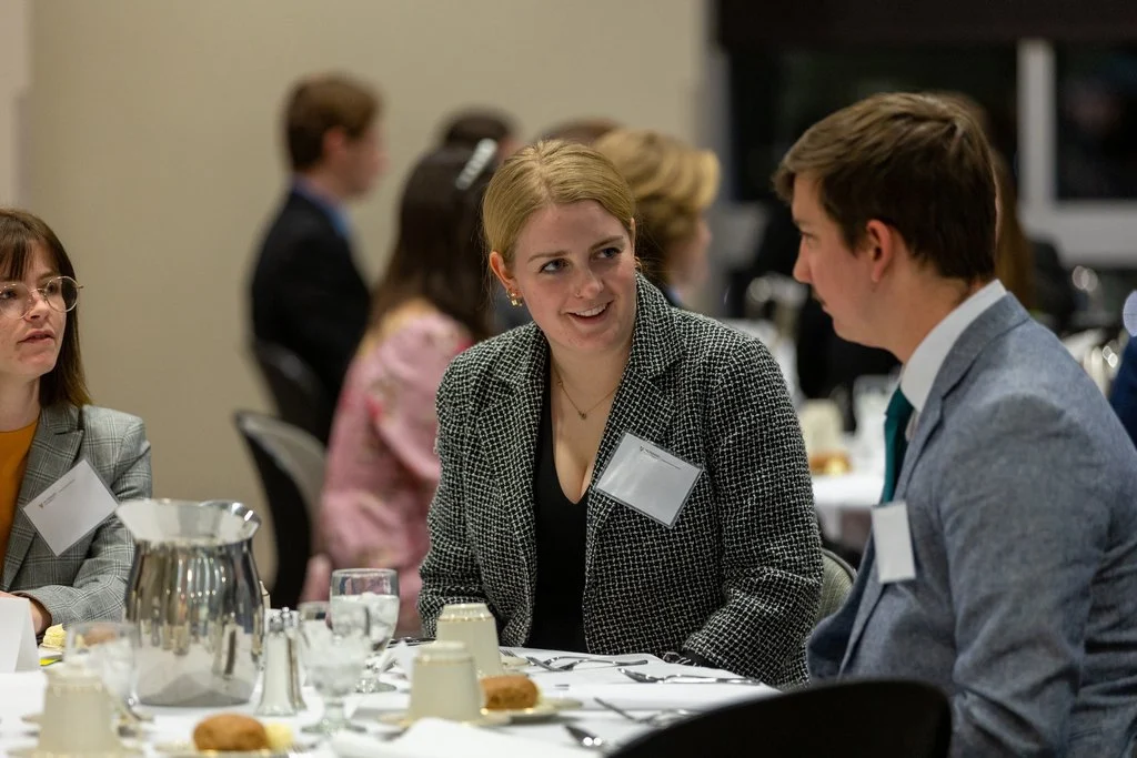 Three people in business attire discuss career guidance while sitting at a dinner table.