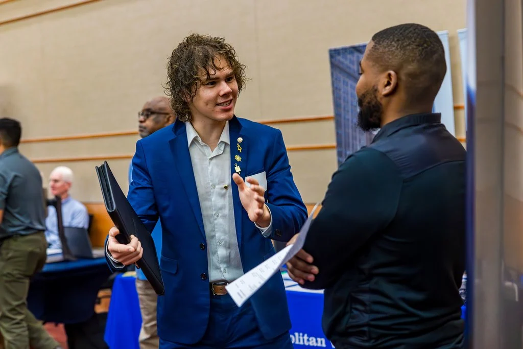 Two men in business attire discuss career development at a professional event.